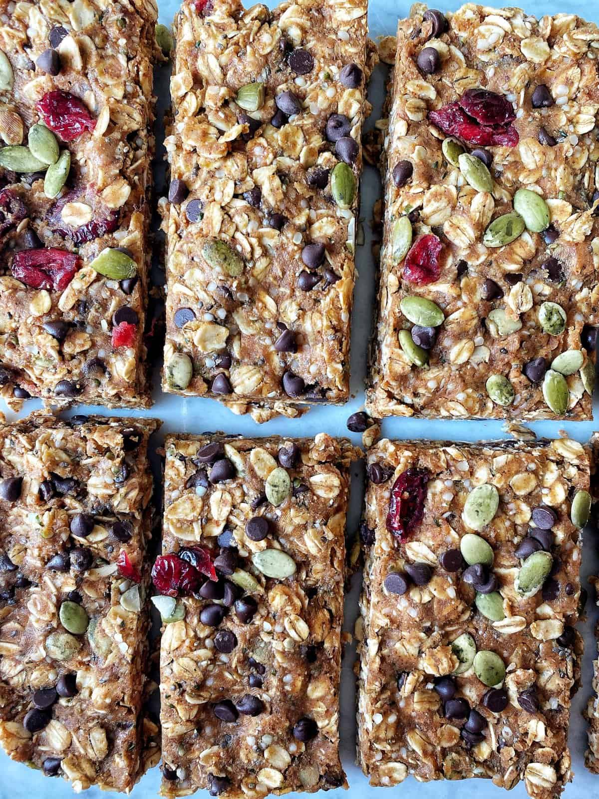 Chewy granola bars with oats, seeds, dried cranberries, and chocolate chips on a baking sheet.