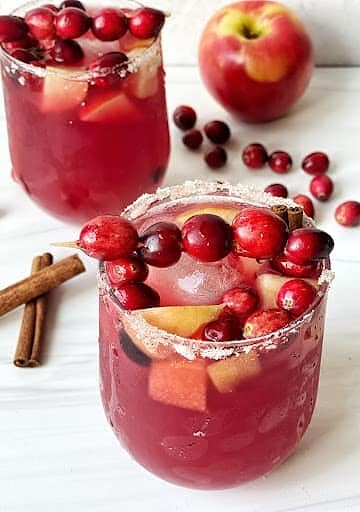 Fresh cranberry apple drinks served in glasses with cinnamon sticks and apple slices, perfect for holiday beverages.