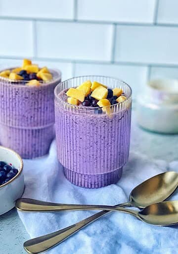Vegan blueberry smoothie in textured purple glasses topped with banana slices.