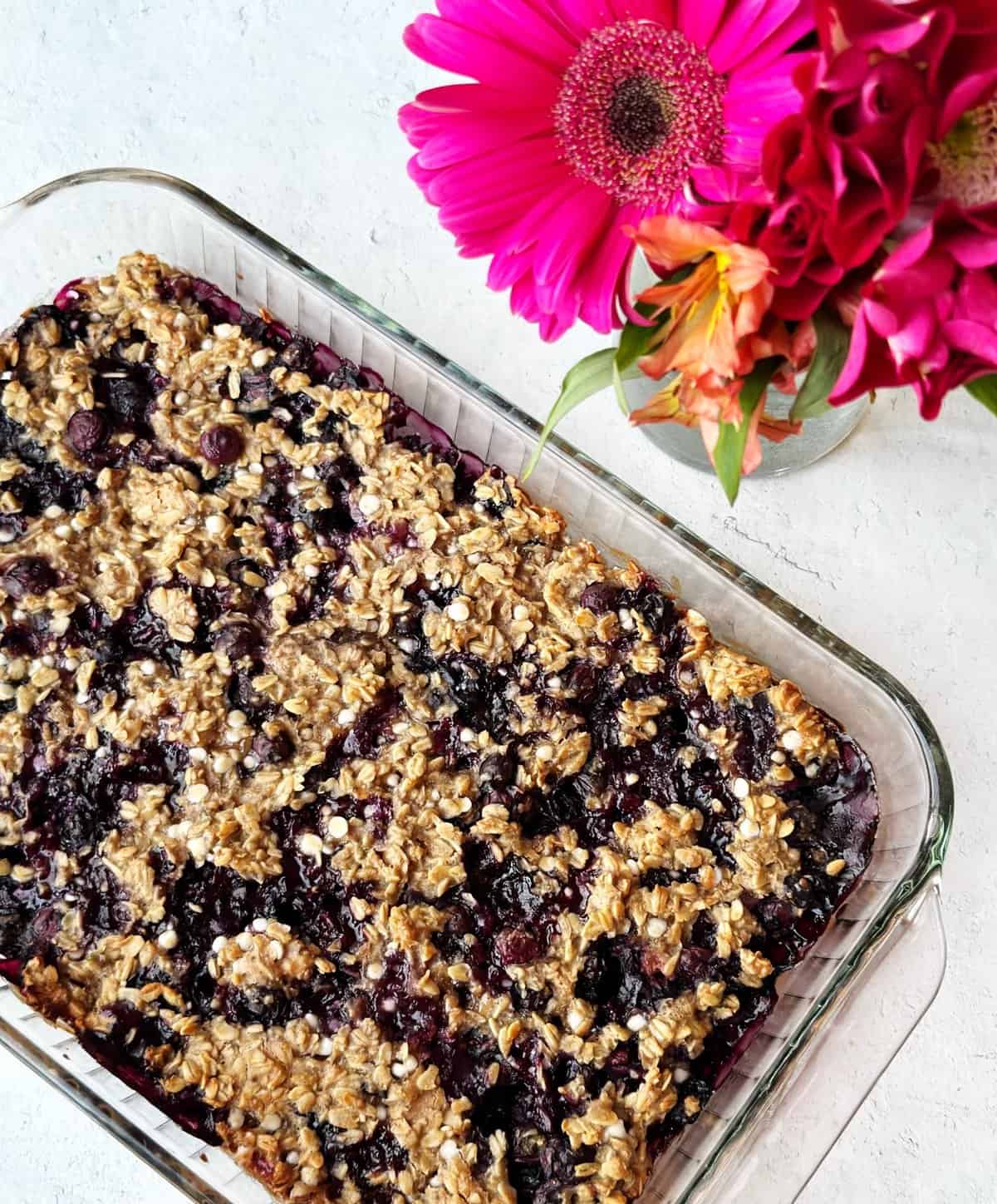 Oatberry crumble dessert in glass dish with pink flowers on white background.