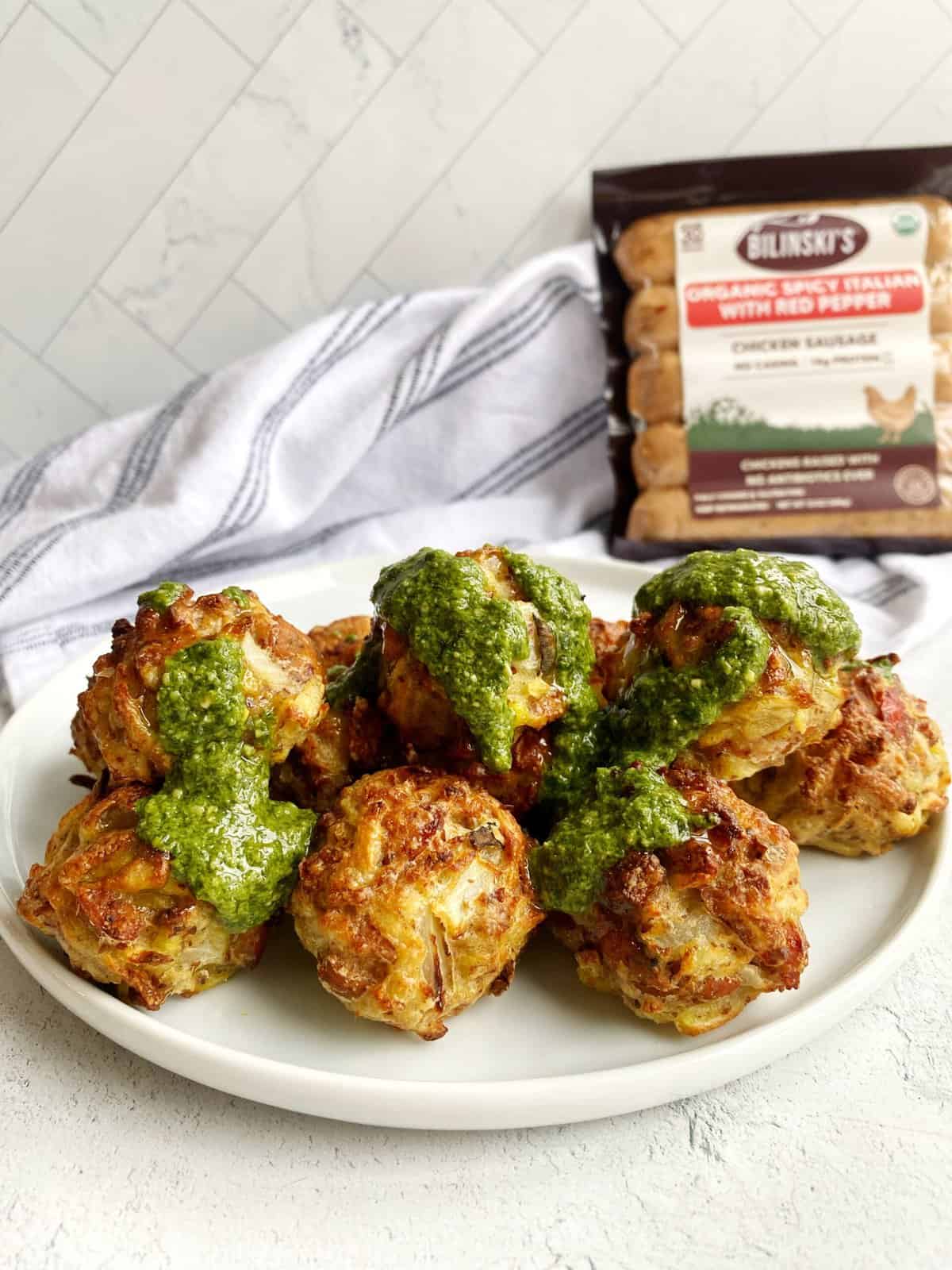 Crispy chicken meatballs with green pesto sauce on white plate.