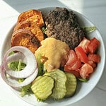 Crispy veggie burger salad with roasted sweet potatoes, cucumbers, tomatoes, red onions, and tahini dressing.