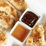 Coconut fried chicken tenders with dipping sauces on a white plate.