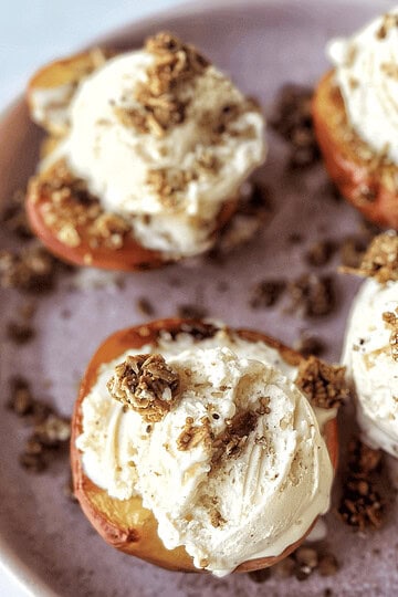 Sweet peach halves topped with vanilla ice cream and granola, served on a pink plate.