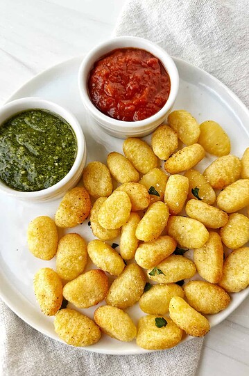 Golden crispy potato bites served with green and red dipping sauces on a white plate.