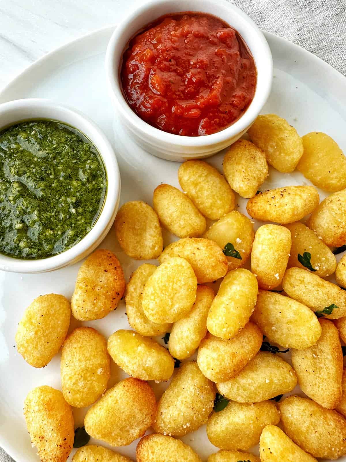 Crispy tater tots with green salsa and red salsa in small bowls, served on a white plate.