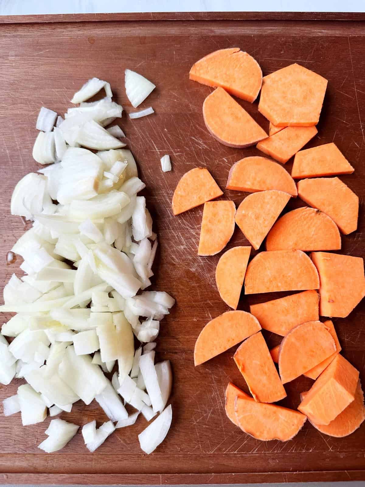 Sliced onions and sweet potatoes on a wooden cutting board