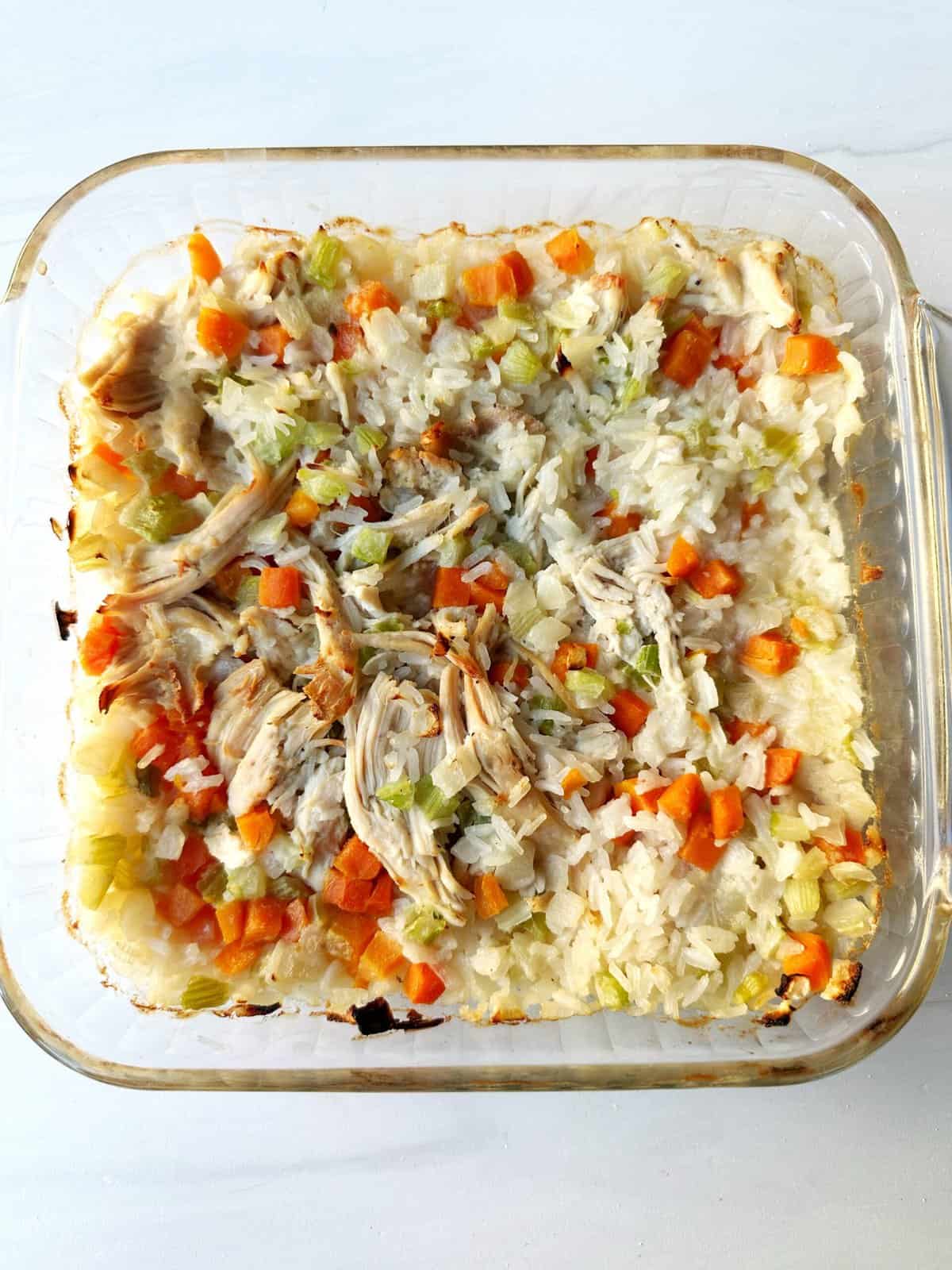 Creamy chicken and rice casserole with mixed vegetables in a glass baking dish.