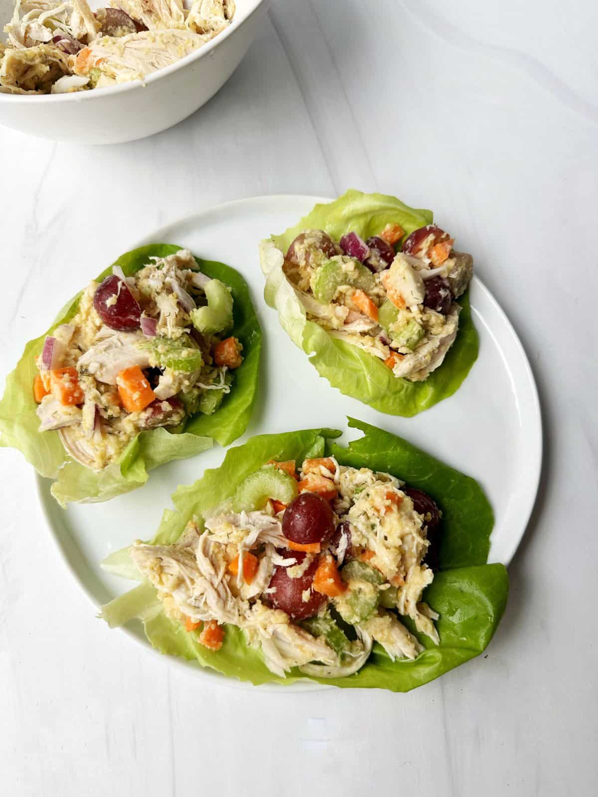 Fresh chicken salad lettuce boats with grapes, celery and carrots on white plate.