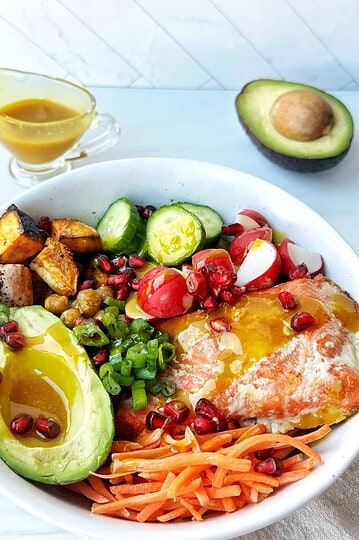 Fresh healthy Buddha bowl with avocado, grilled sweet potatoes, cherry tomatoes, radishes, and cucumbers.