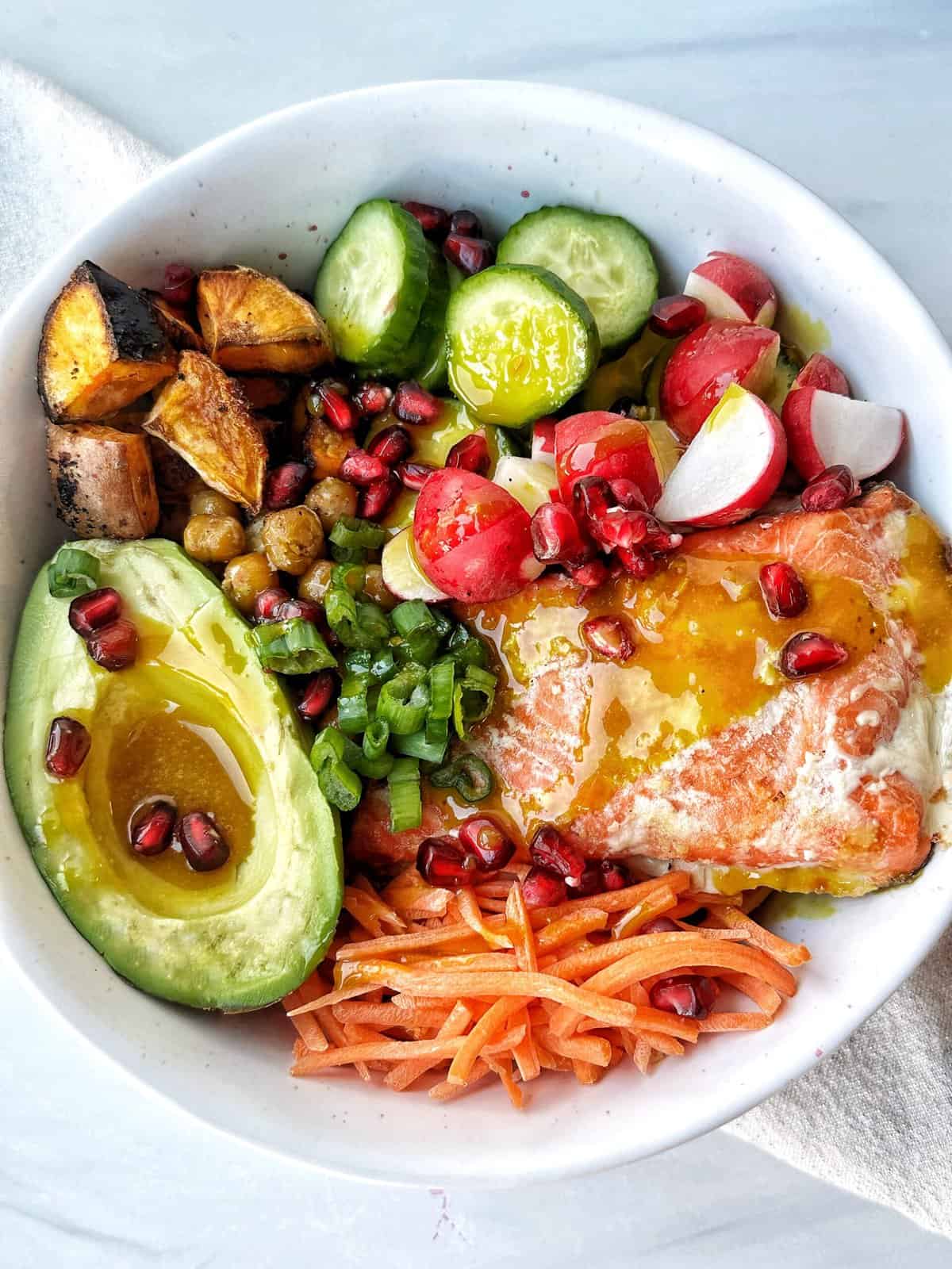 Fresh colorful healthy meal bowl with avocado, cucumber, radishes, sweet potato, pomegranate seeds, and eggs.