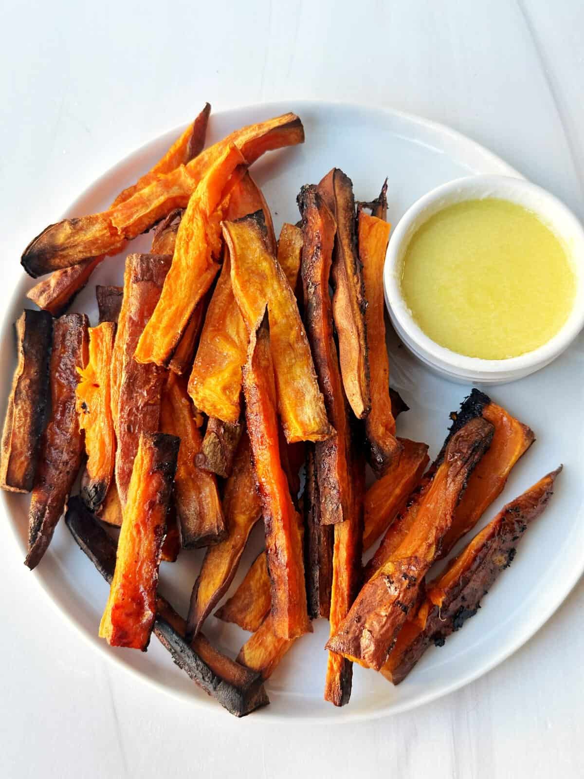 Baked sweet potato fries with dipping sauce on a white plate.