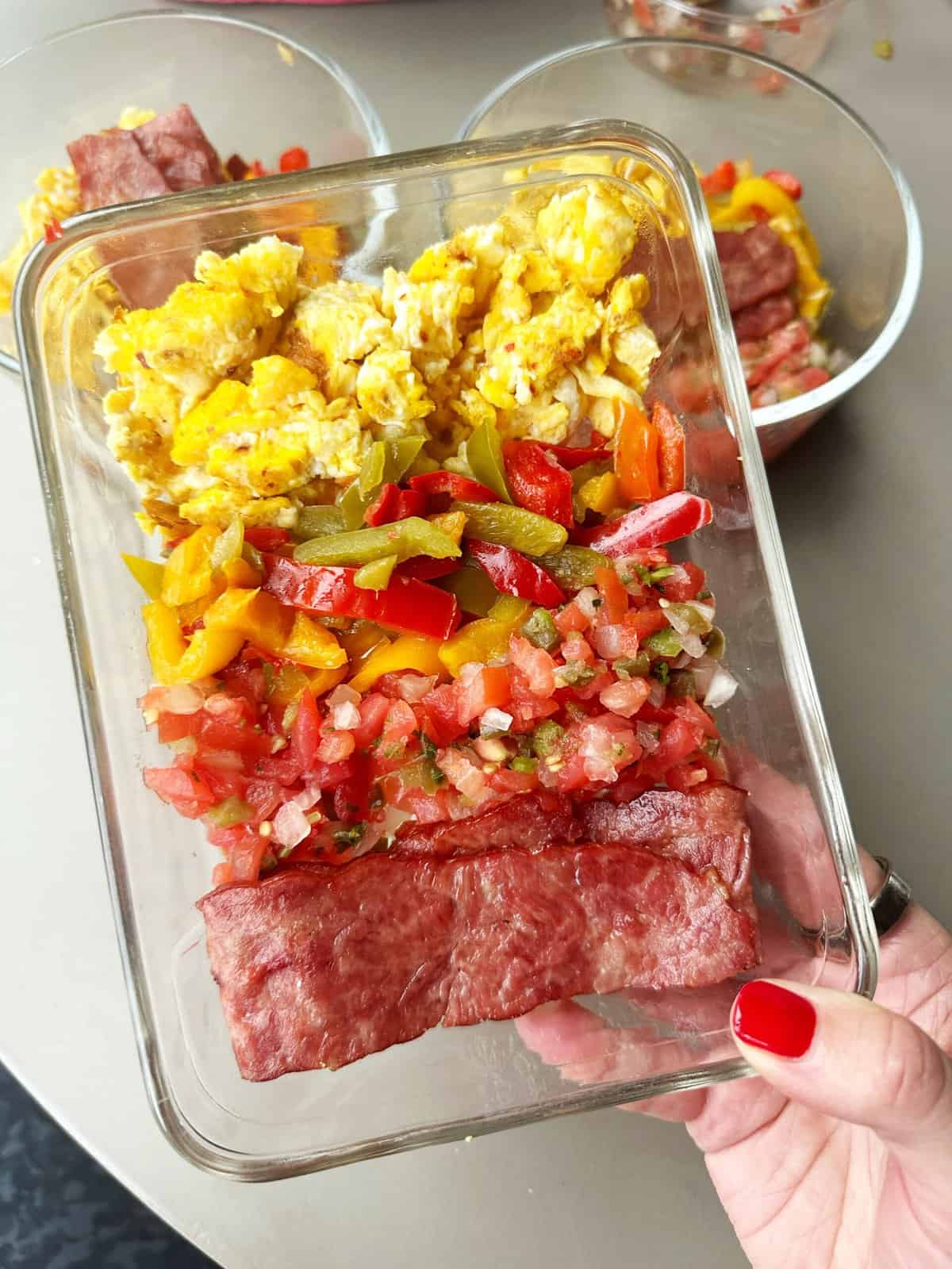 Scrambled eggs with colorful vegetables in glass meal prep container.