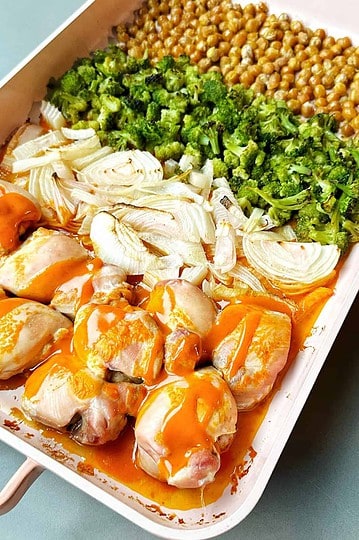 Juicy chicken thighs with melted mozzarella, fresh vegetables, and flavorful sauce arranged in a white baking dish.