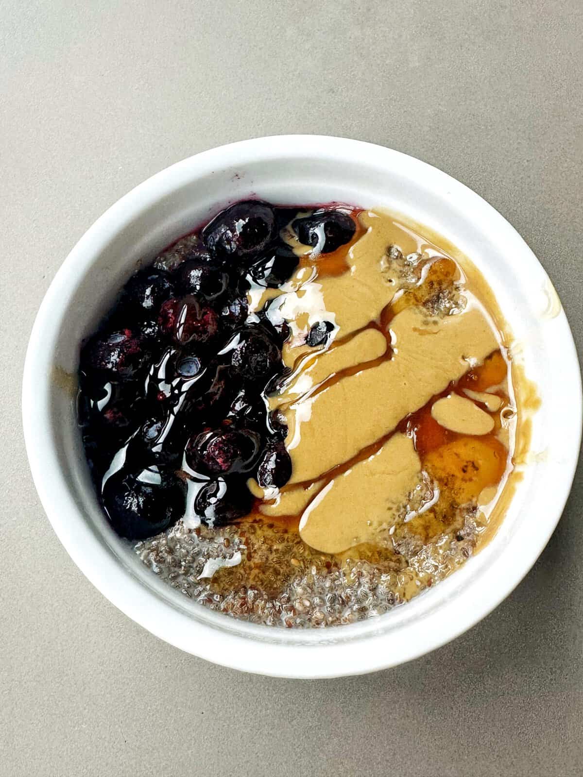 Fresh blueberry smoothie bowl with honey, peanut butter, and chia seeds on a gray background, healthy breakfast recipe.