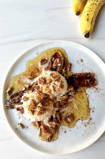 Fresh banana foster with ice cream topped with chopped pecans on a white plate.