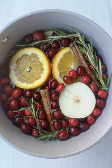 Fresh fruit infusion with orange, apple, cranberries, rosemary, and cinnamon sticks in a water pitcher for healthy hydration.
