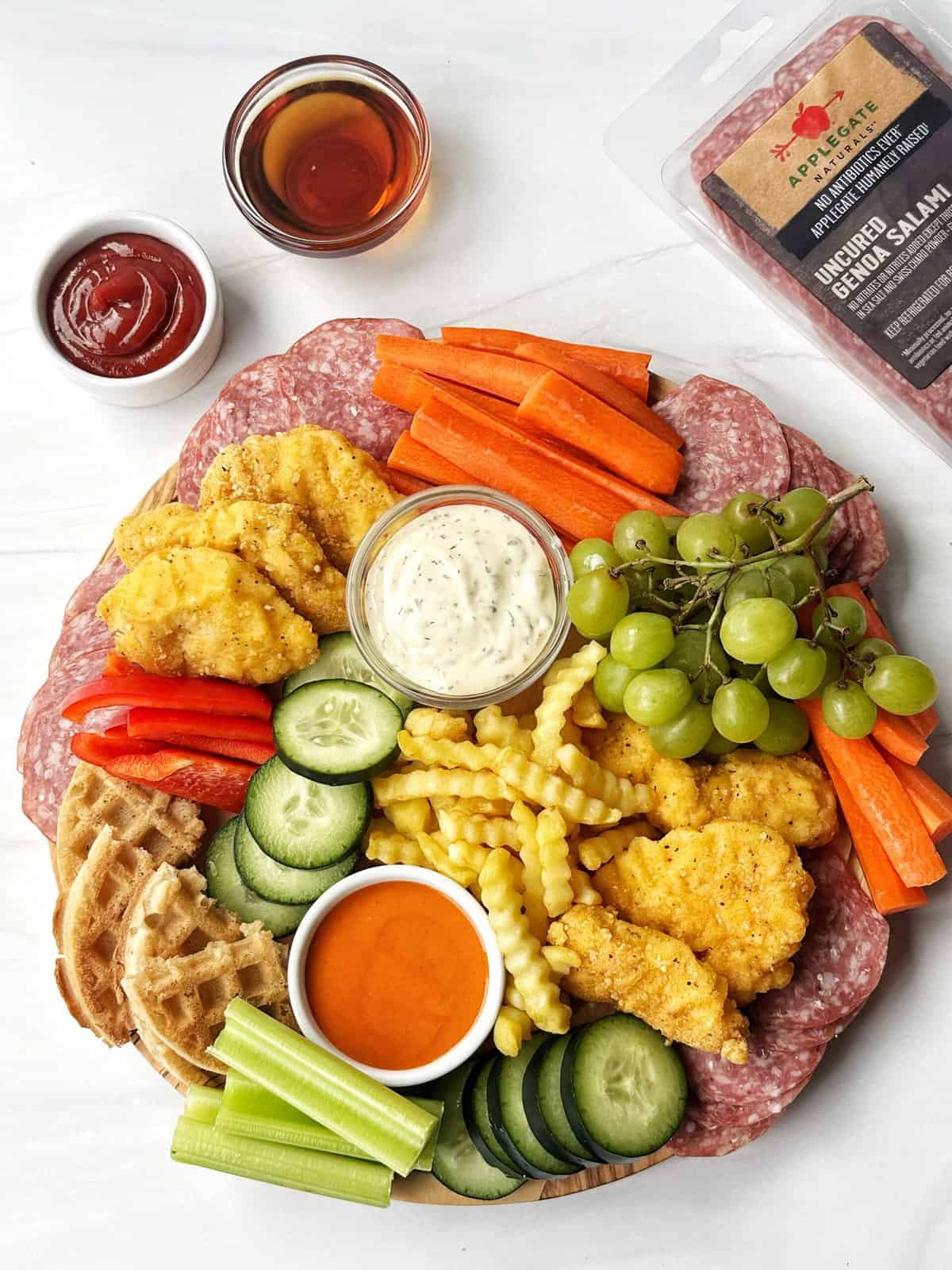 Fresh plant-based charcuterie board with vegetables, dips, and vegan salami from Lesswithlaur. Perfect for healthy snacking and grazing.
