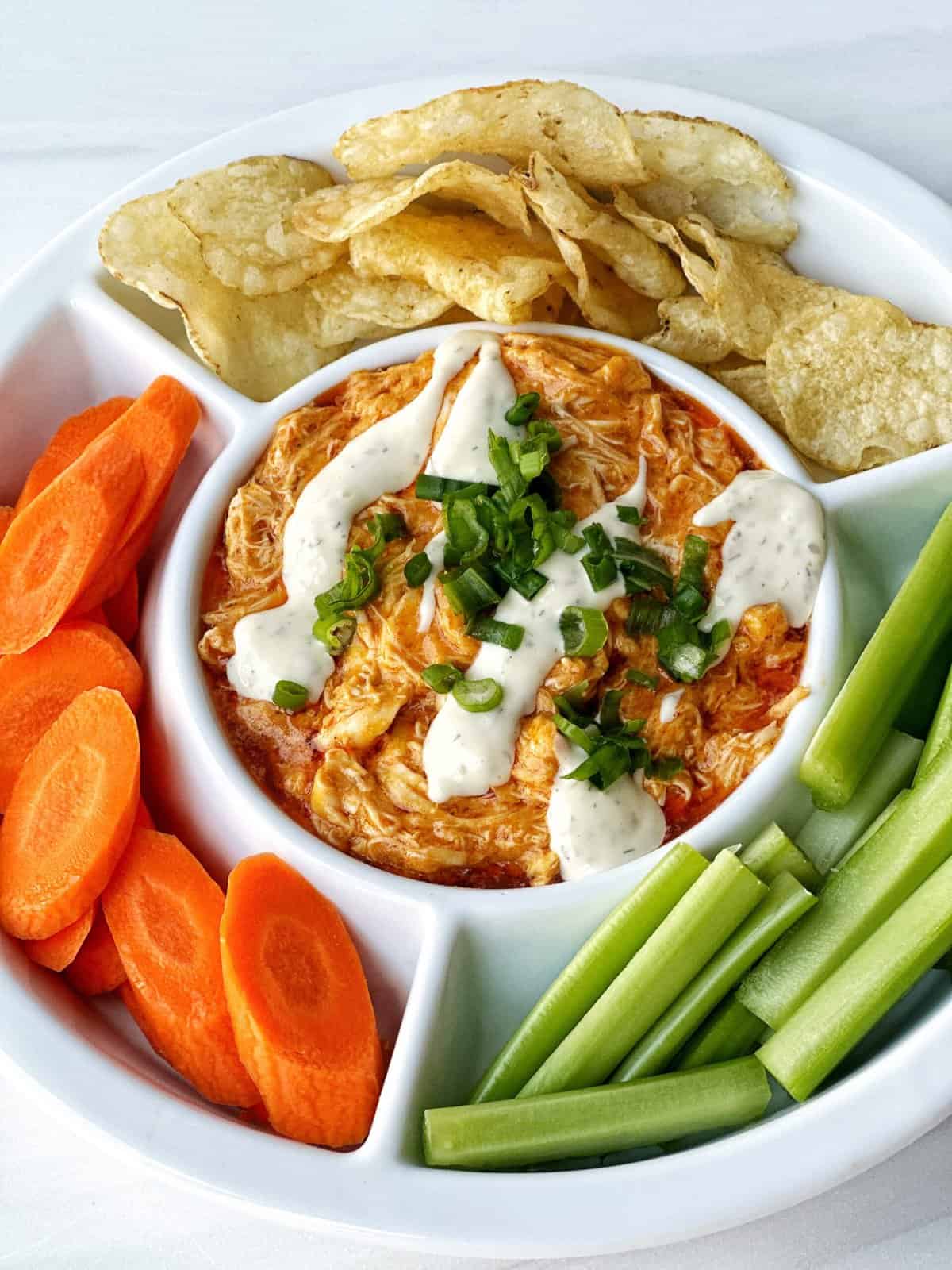 creamy dairy-free buffalo chicken dip served with celery, carrots and chips on a white platter