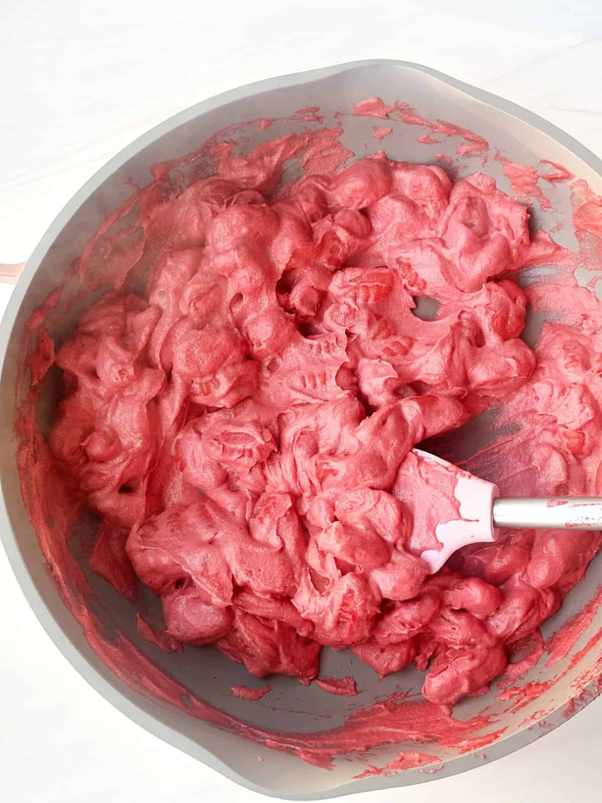Bright pink homemade whipped soap mixture in a mixing bowl with spatula, ready for skincare or DIY beauty project.