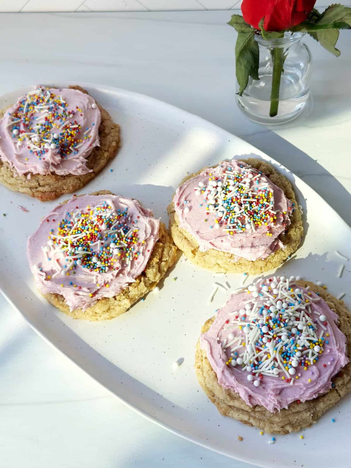 Colorful sugar cookies with pink frosting and rainbow sprinkles on a white platter.