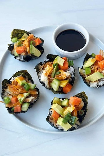Sushi rolls with fresh vegetables and drizzle of soy sauce on white plate.