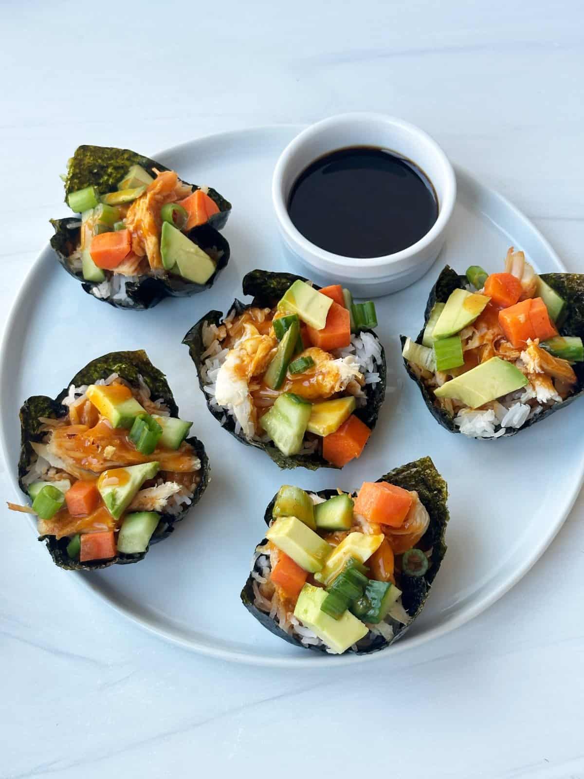 Sushi rolls with fresh vegetables and drizzle of soy sauce on white plate.