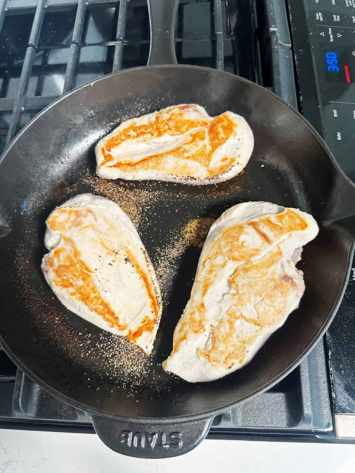 Sizzling chicken breasts cooking in a cast iron skillet on stove.