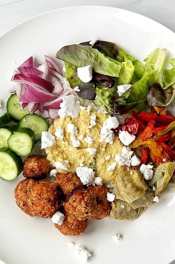 Fresh Greek salad with falafel, hummus, and feta cheese, served on a white plate.