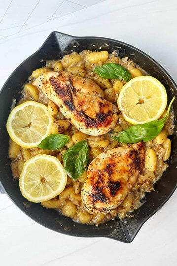 Roasted chicken with lemon and basil served over gnocchi in skillet.