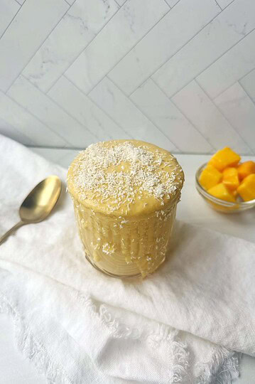 Creamy mango chia pudding topped with shredded coconut, served in a glass jar against a white marble background.