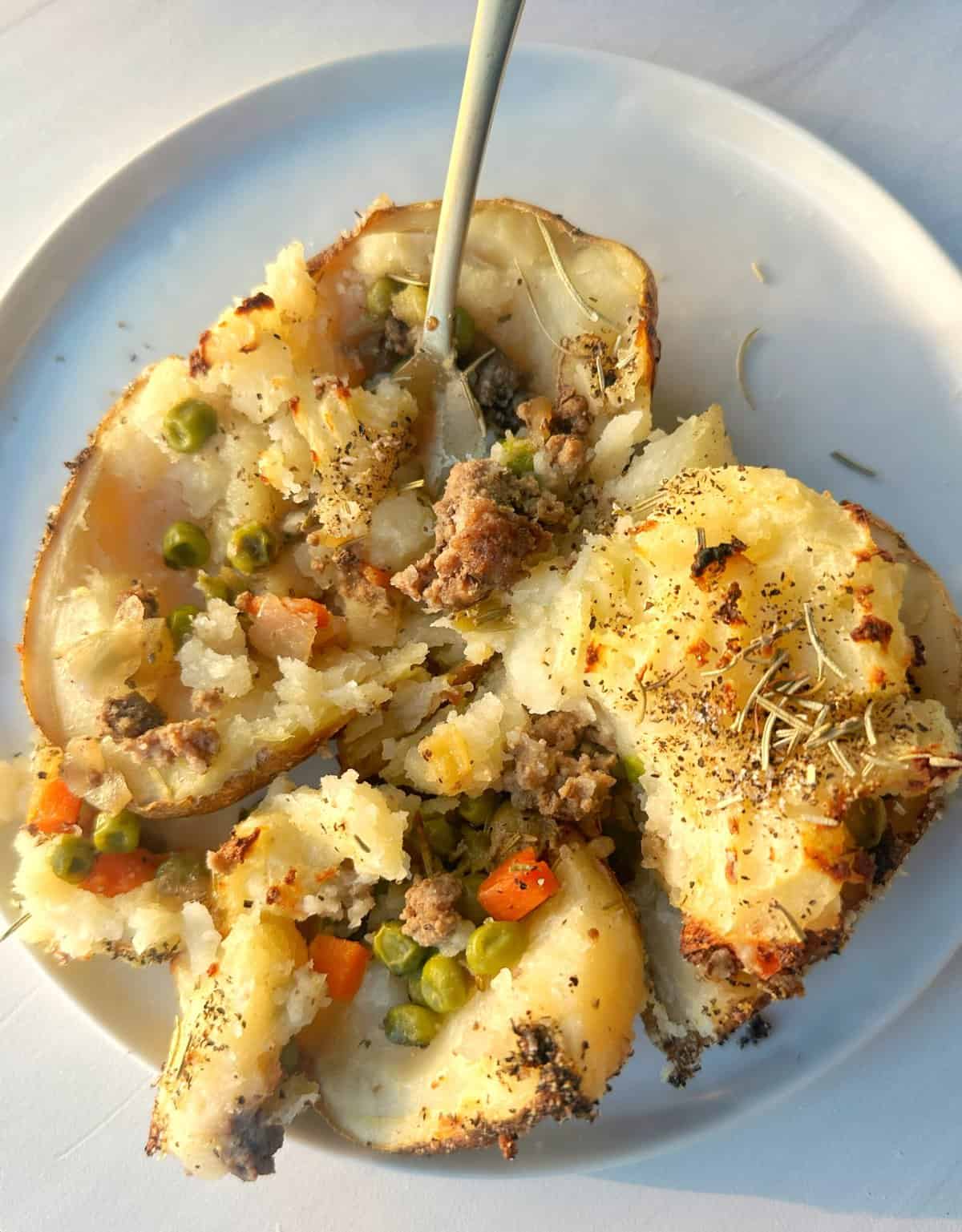 Mashed potato casserole with ground beef, peas, carrots, and herbs on white plate.
