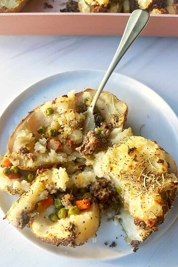 Roasted potato with ground meats and vegetables, baked to perfection, served on a white plate.