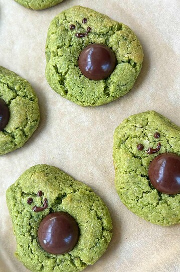 Chocolate smiling face cookies with green icing on parchment paper.
