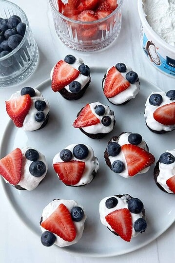 Fresh chocolate cupcakes topped with whipped cream and strawberries and blueberries.