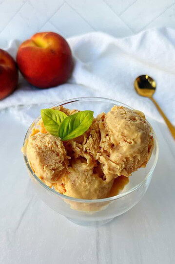 Creamy peach ice cream in a glass bowl with fresh basil garnish. Perfect summer dessert with fresh peaches and smooth texture.
