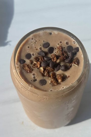 Creamy chocolate protein smoothie with chocolate chips and granola topping.