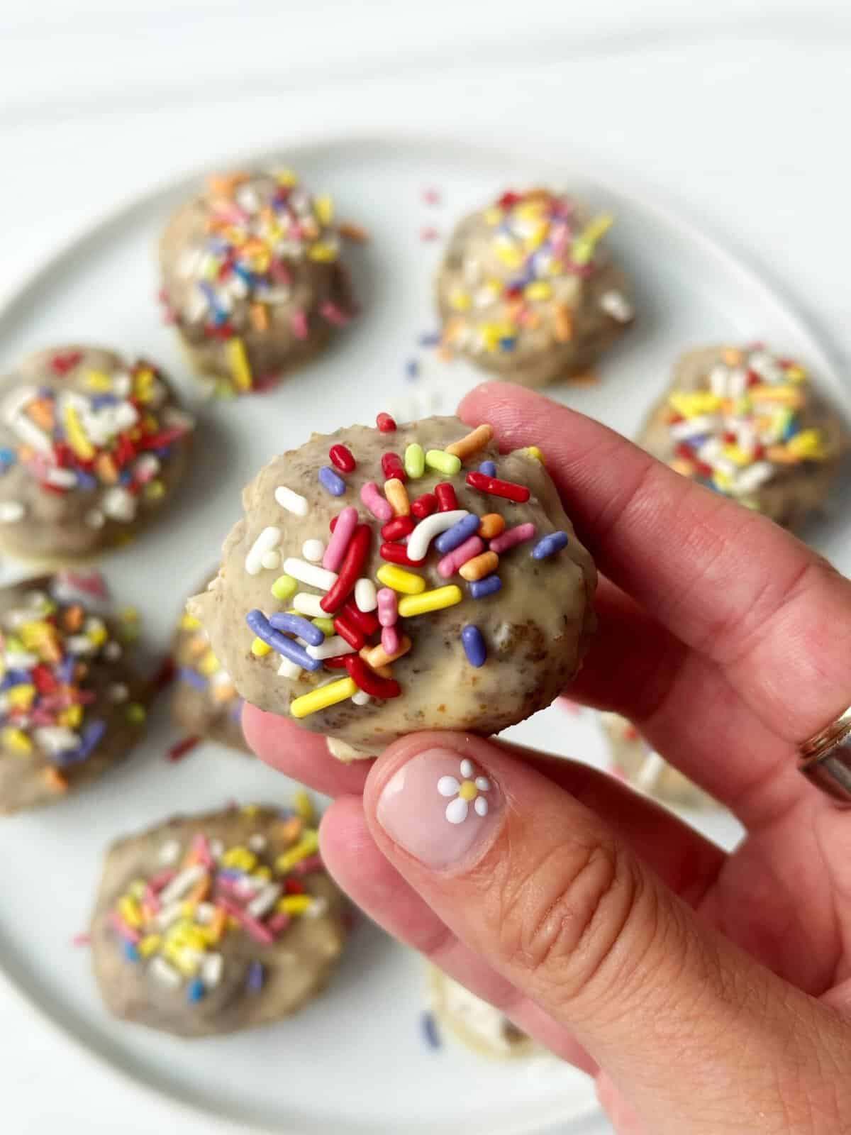 Colorful baked mini donuts with rainbow sprinkles on a white plate, perfect for sweet snacks or celebrations.