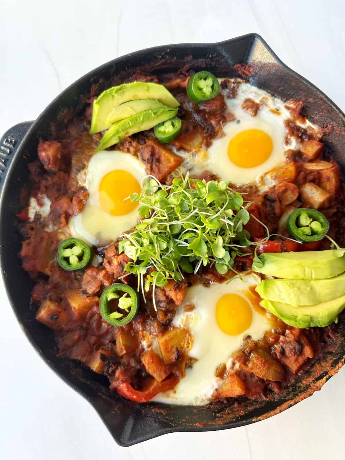 Savory breakfast skillet with eggs, avocado, microgreens, and peppers on a black cast iron skillet.
