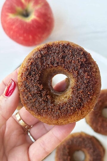 Crunchy cinnamon sugar apple cider donut close-up with a red apple in the background, perfect for fall recipes.