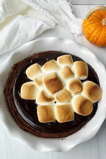 Marshmallow-topped s'mores pie with chocolate filling on white plate.