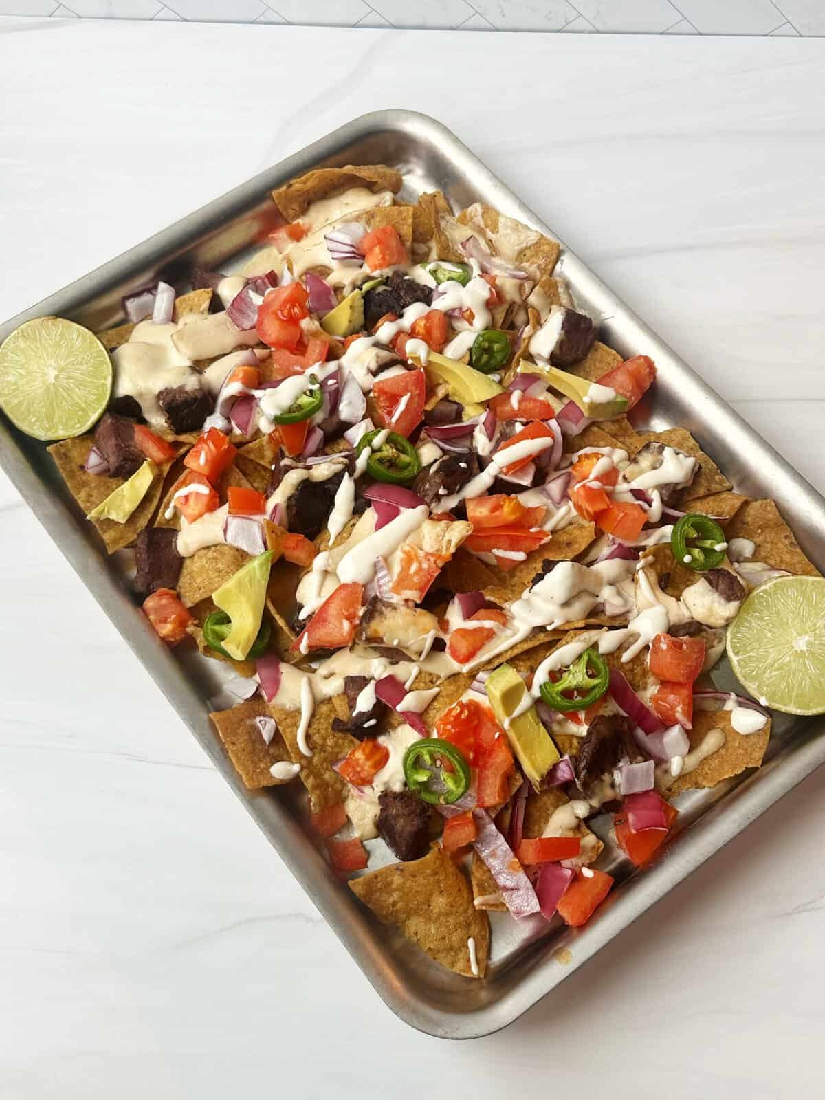 Crispy nachos topped with fresh vegetables, cheese, and sour cream on a metal tray.