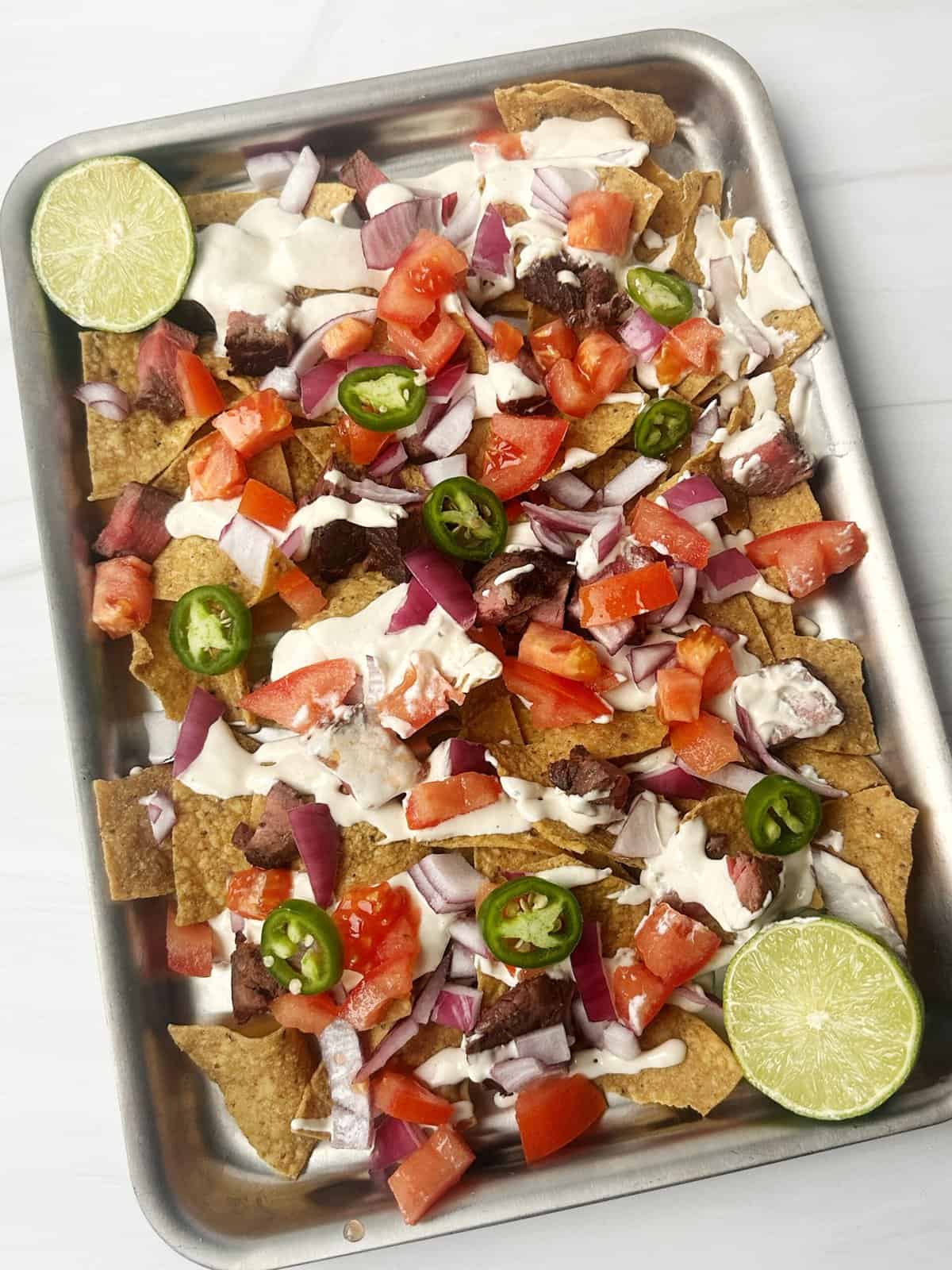 Crispy beef taco platter topped with fresh tomatoes, onions, jalapeños, and drizzled with creamy sauce, garnished with lime slices.