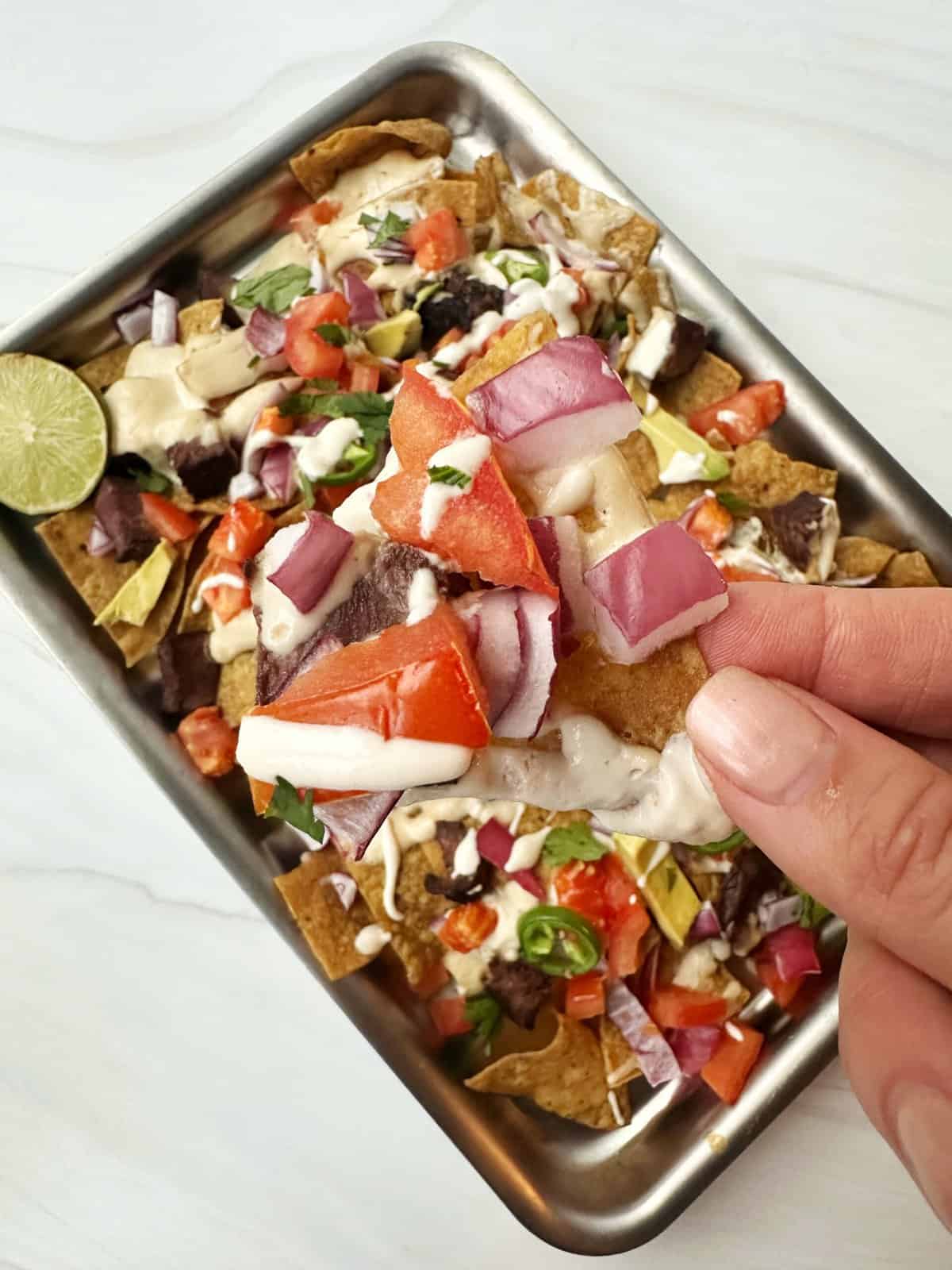 Crunchy nachos topped with fresh vegetables, sour cream, and jalapeños on a metal tray.