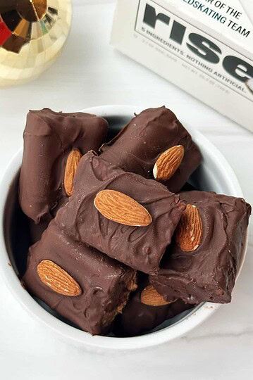 Decadent chocolate almond fudge squares in a white bowl on a white surface.