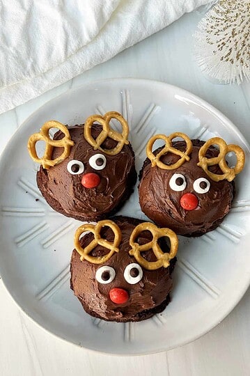 Cute reindeer-shaped chocolate cupcakes decorated with pretzels, candy eyes, and red candy noses, perfect for holiday desserts.