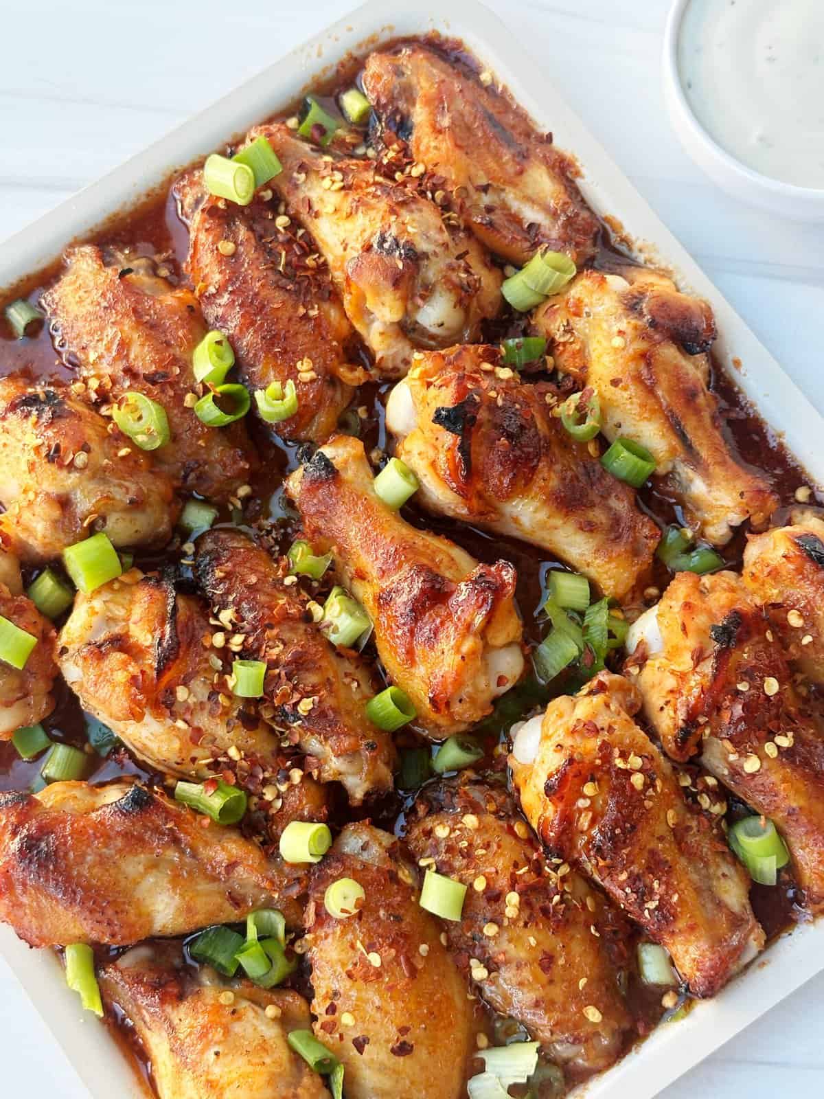 Crispy baked chicken wings topped with green onions and crushed red pepper flakes in a savory sauce.
