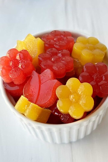 Vegan gummy candies in a white bowl, colorful and fruit-flavored, on a white surface.