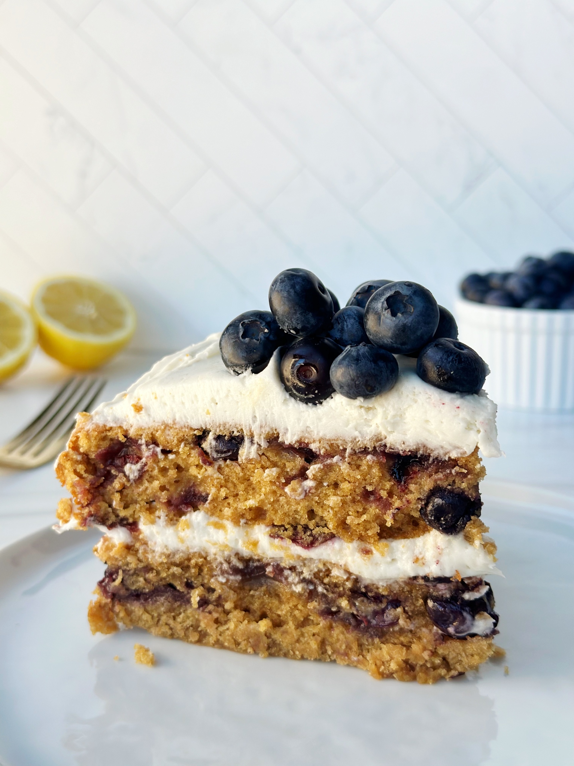 Fresh blueberry crumble cake with creamy frosting and lemon slices in the background.