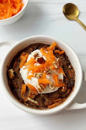 Delicious baked good topped with whipped cream, orange zest, and chopped nuts in a white mug.